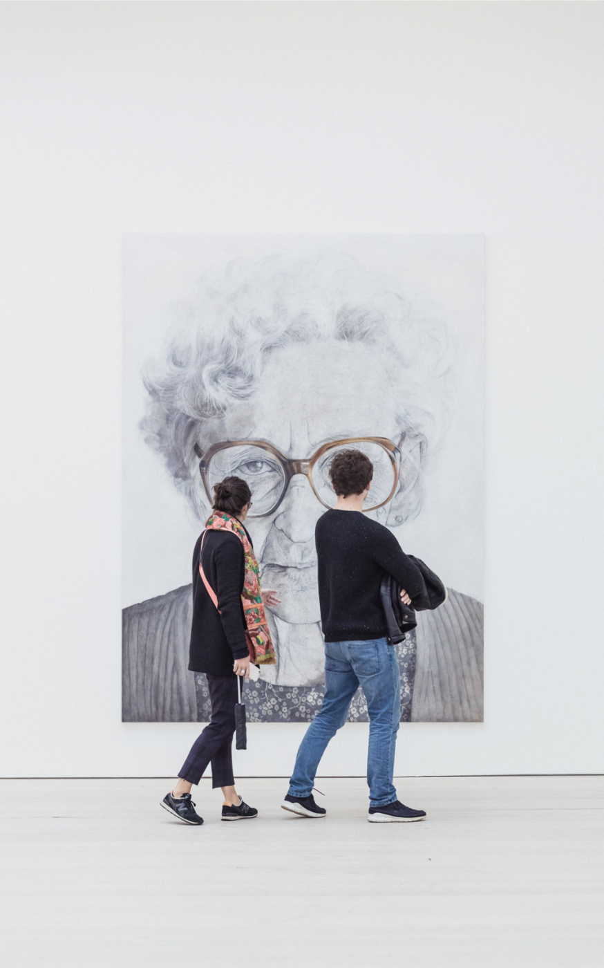 Two people viewing a large portrait in a modern art gallery